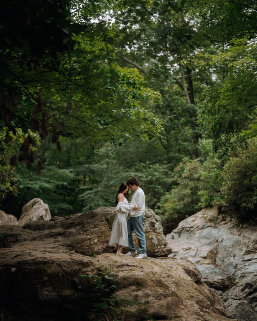 Destination engagement photos at Trash Can Falls in the Blue Ridge Mountains, with overcast skies, lush forest, and romantic waterfall backdrops. Captured by destination wedding and engagement photographer KNCAPTURES