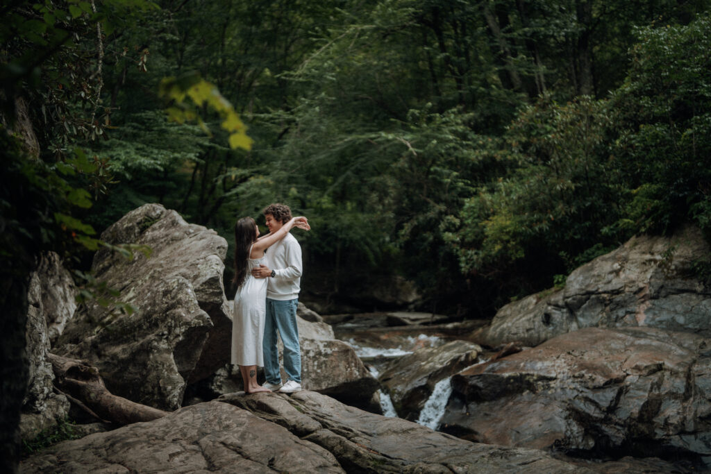 Destination engagement photos at Trash Can Falls in the Blue Ridge Mountains, with overcast skies, lush forest, and romantic waterfall backdrops. Captured by destination wedding and engagement photographer KNCAPTURES
