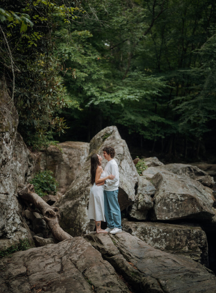 Destination engagement photos at Trash Can Falls in the Blue Ridge Mountains, with overcast skies, lush forest, and romantic waterfall backdrops. Captured by destination wedding and engagement photographer KNCAPTURES