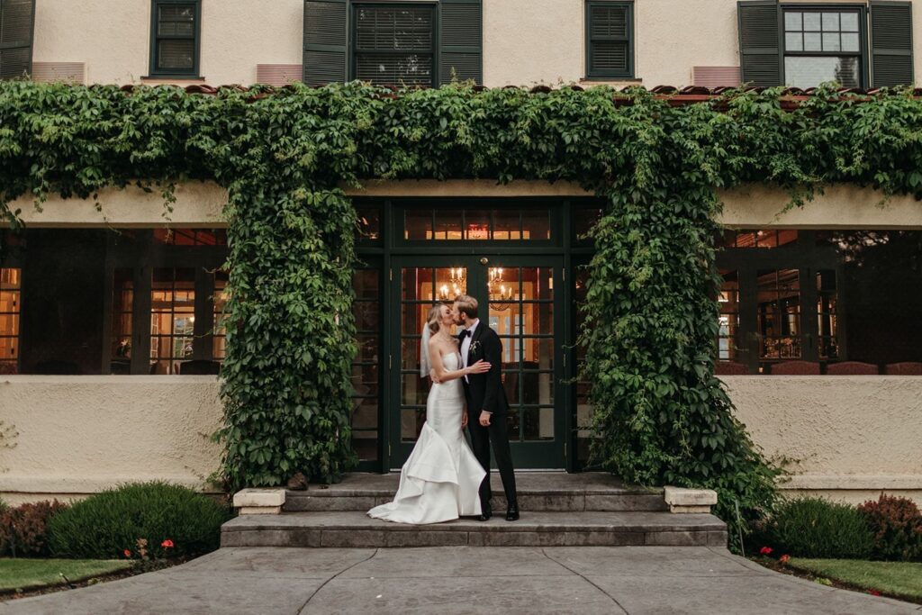 Columbia Gorge Hotel and Spa wedding in Hood River Oregon — historic venue with waterfall views, manicured gardens, and elegant on-site lodging Couple kissing in front of the reception hall.